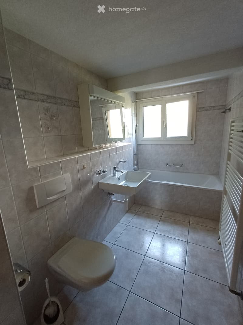Modern bathroom with tiled walls and floor, featuring a toilet, sink, bathtub, mirror, and radiator.
