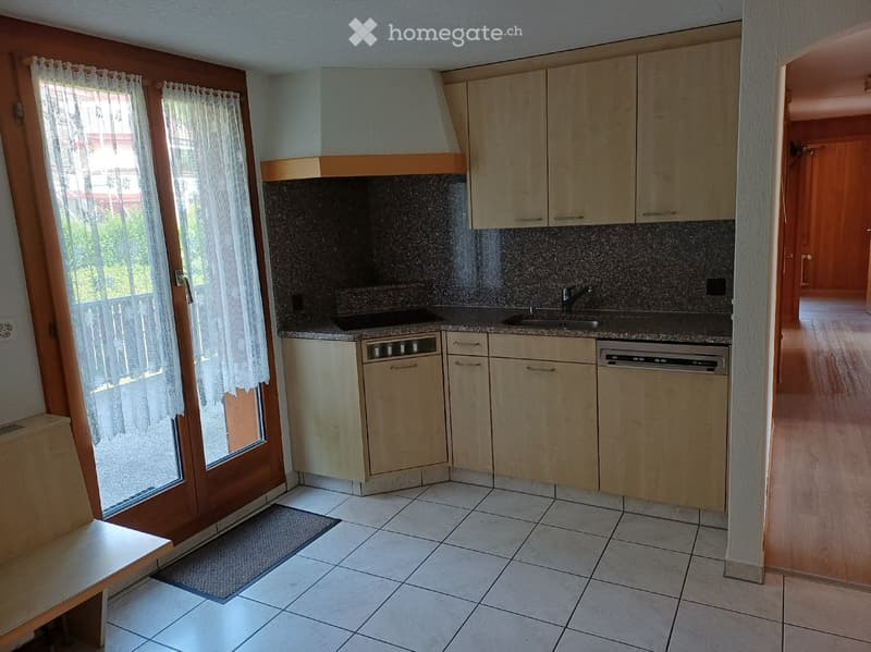 Modern kitchen with light wooden cabinets, granite countertop, sink, and dishwasher. Features a large window with white lace curtains and a tiled floor.