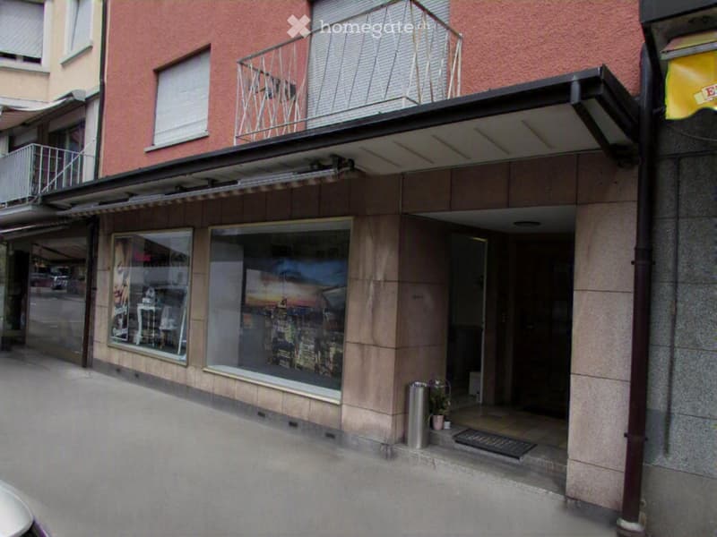 Building exterior with a balcony, awning, and storefront windows displaying posters and images.