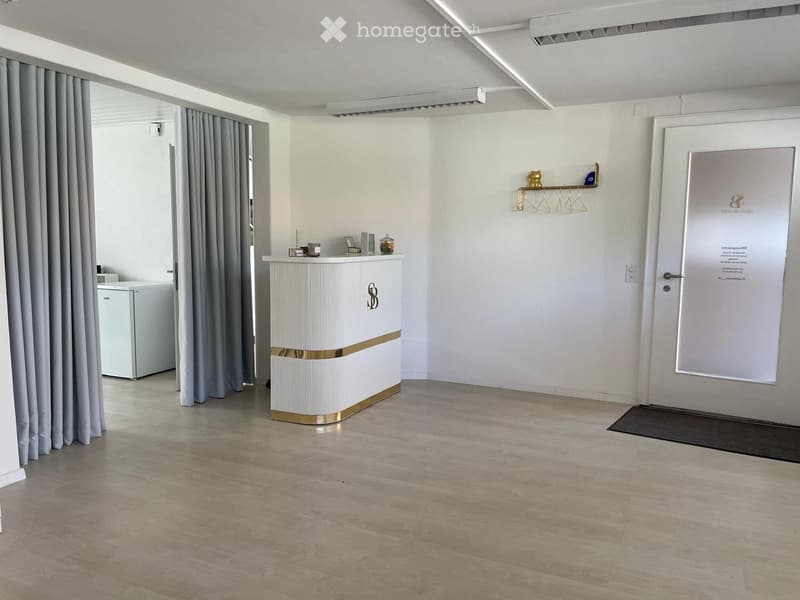 Modern reception area with a white reception desk, small refrigerator, coat rack, and decorative items on the desk.