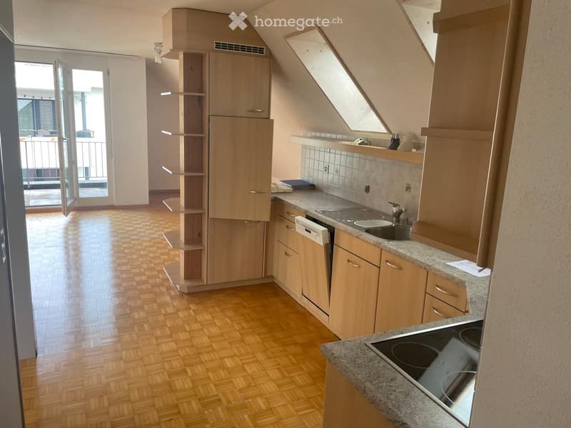 Modern kitchen with wooden cabinets, granite countertops, electric stove, sink, and dishwasher. The space features a slanted ceiling with a skylight and an open doorway leading to a balcony.