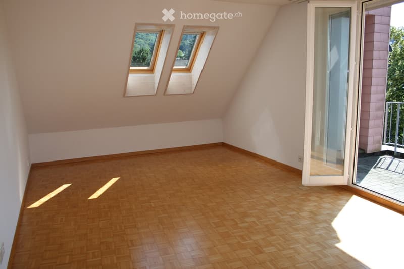 Empty attic room with wooden flooring, slanted ceilings, and two skylights. Features a large glass door leading to a balcony.