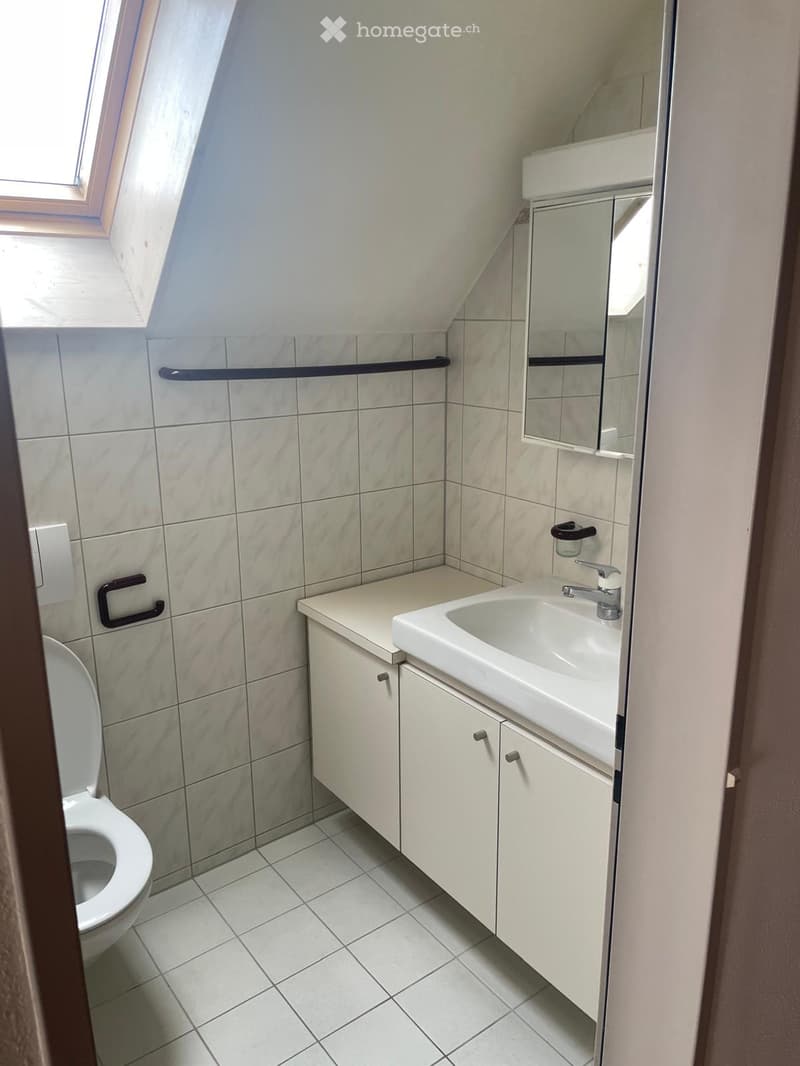 Modern bathroom with white tiles, a toilet, a sink with a mirror, and a small cabinet.