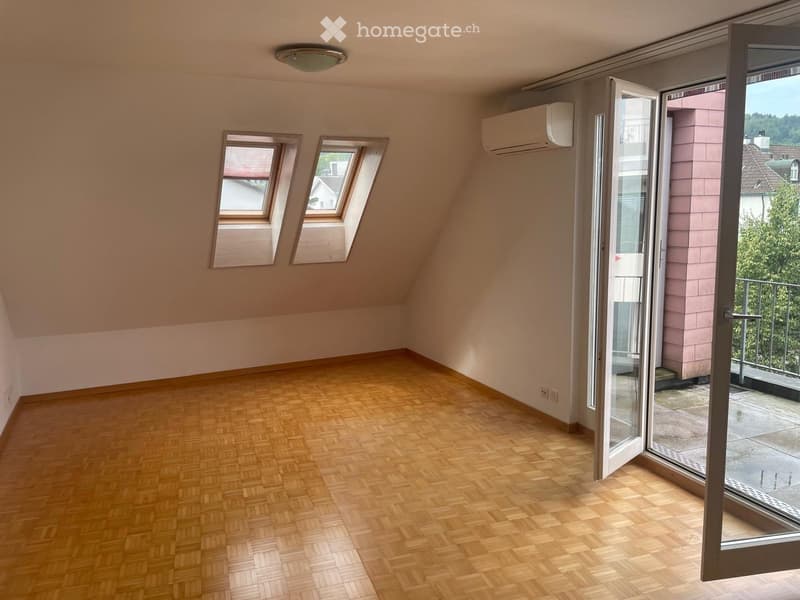 Empty attic room with wooden flooring, slanted ceilings, two skylights, and a large sliding glass door leading to a balcony.