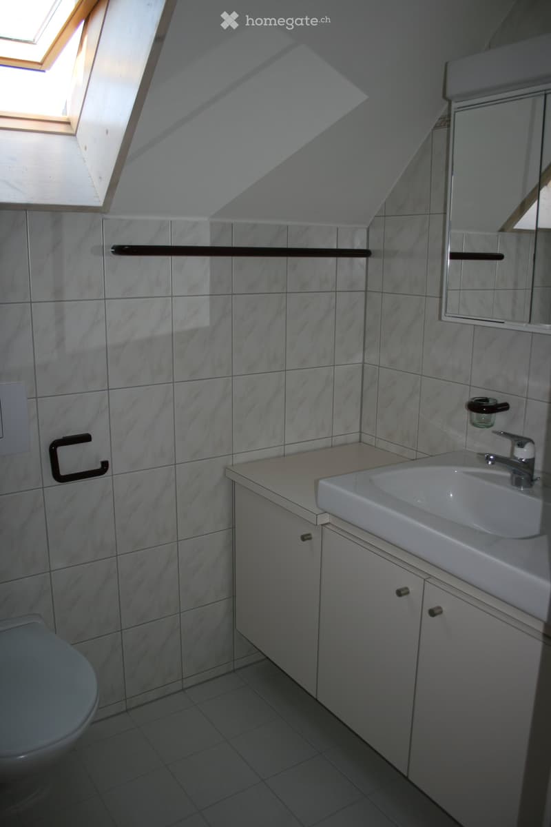 Modern bathroom with white tiles, a sink, toilet, mirror, and built-in cabinetry.