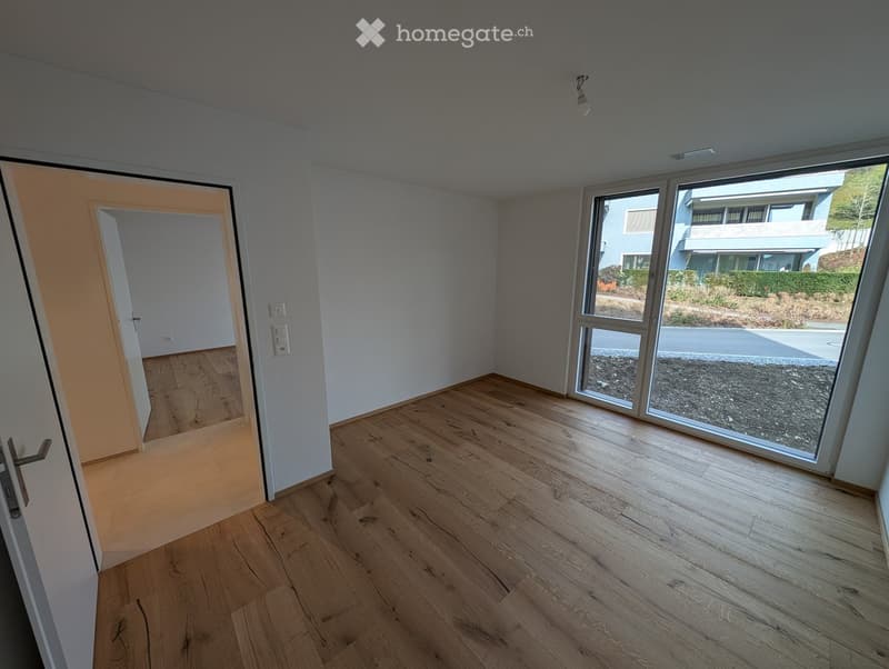 Empty room with light wooden flooring, white walls, and large glass sliding doors leading to an outdoor area.