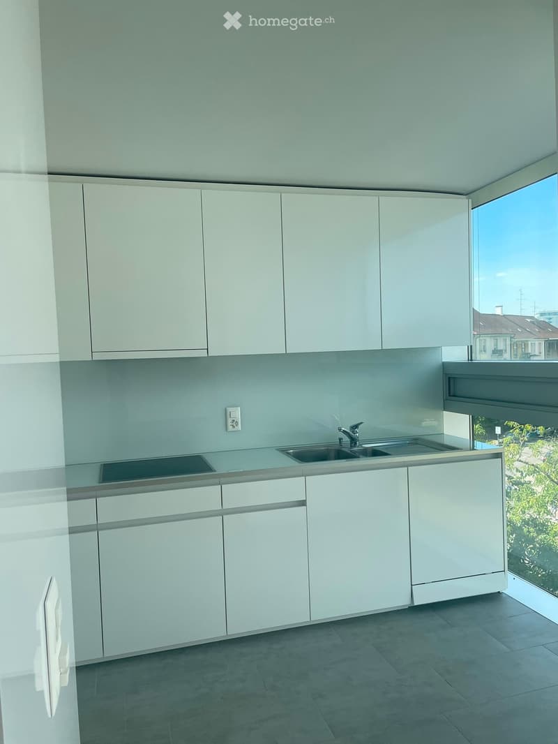 Modern kitchen with white cabinets, light grey countertops, and a double sink. Large windows provide natural light and a view of the outdoors.