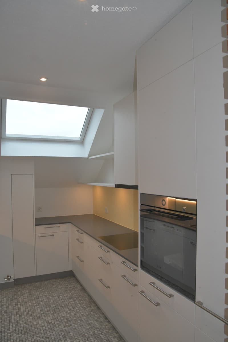 modern kitchen with white cabinets, gray countertop, stainless steel oven, skylight