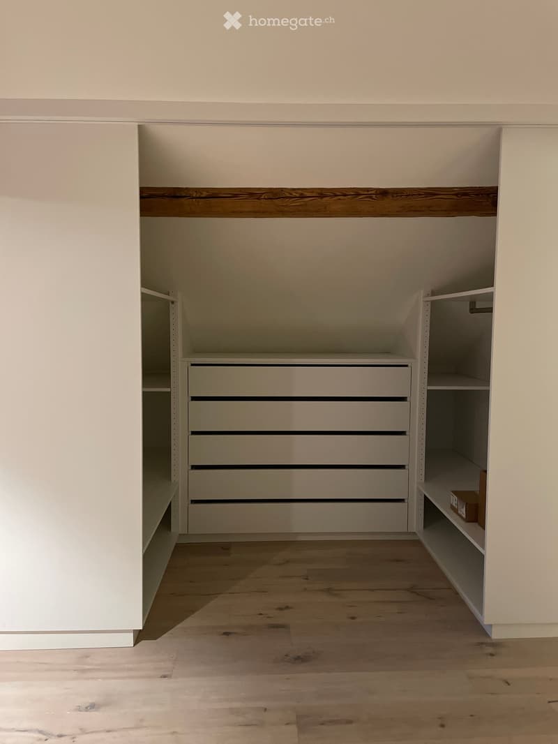 Empty closet with built-in storage including shelves and drawers, light-colored wood flooring, and white walls.