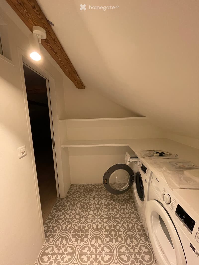 Small laundry room with a washing machine and dishwasher, featuring patterned tile flooring and white walls.