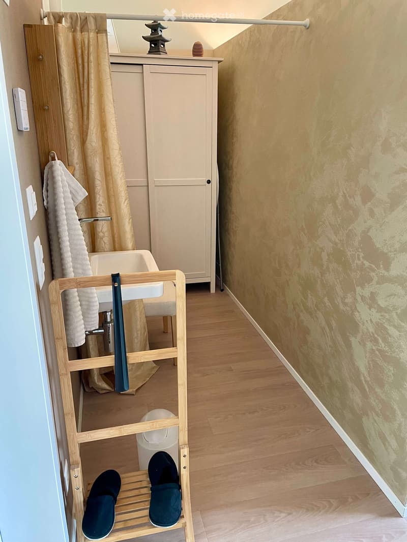 Bathroom with wooden floor, sink, mirror, cabinet, towel rack, and a pair of shoes on a wooden shoe rack.