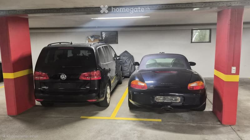 Underground parking area with two cars parked, one a Volkswagen Touran and the other a BMW Z4 convertible, marked parking spaces with yellow lines, red support pillars, and a covered item in the background.
