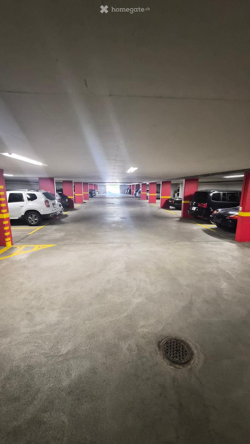 Underground parking lot with several parked cars, red pillars, and yellow markings on the floor.