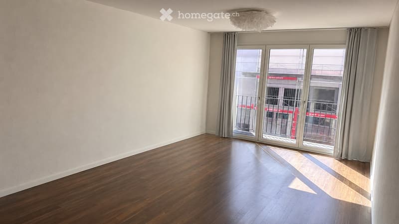 Empty room with wooden flooring, large sliding glass doors leading to a balcony, and light-colored walls.
