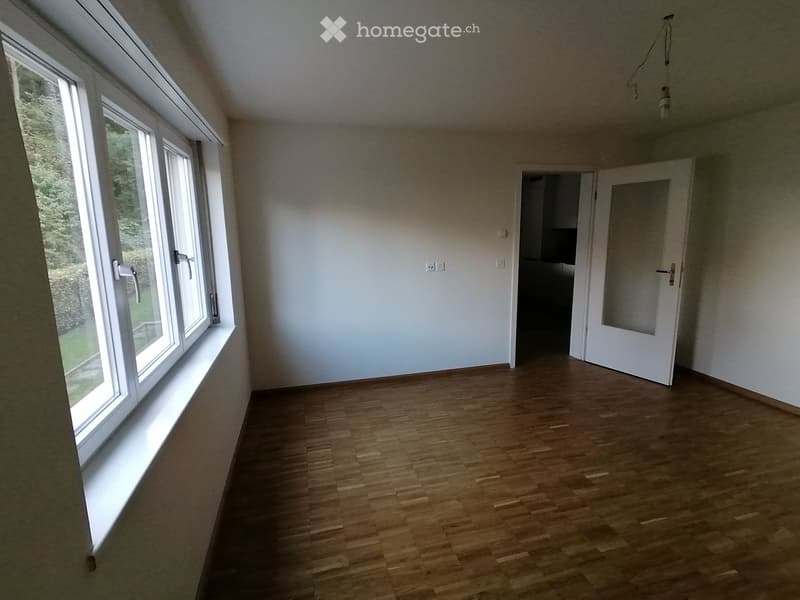 Empty room with wooden flooring, large windows, and a door leading to another space.
