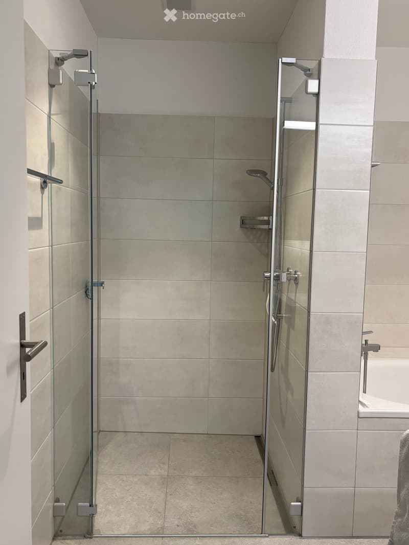 Modern bathroom with a glass-enclosed shower stall, tiled walls and floor, and a sleek chrome faucet.