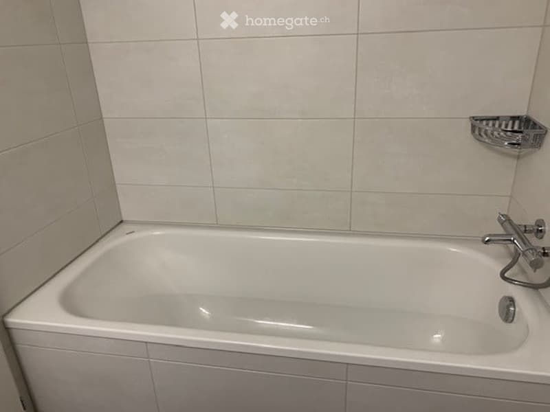 A clean, modern bathroom with a white bathtub, chrome faucet, and a towel rack on the wall.