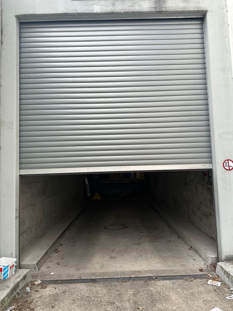 Closed garage door with a small open section revealing a concrete floor and minimal interior space.