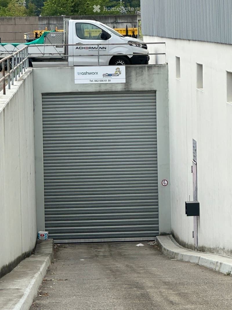 A closed garage door with a sign for a car wash service above it, located between two buildings with a small staircase leading up to it.
