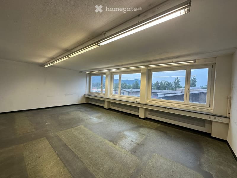 Empty room with concrete floor, large windows, and fluorescent lighting. No furniture or equipment present.