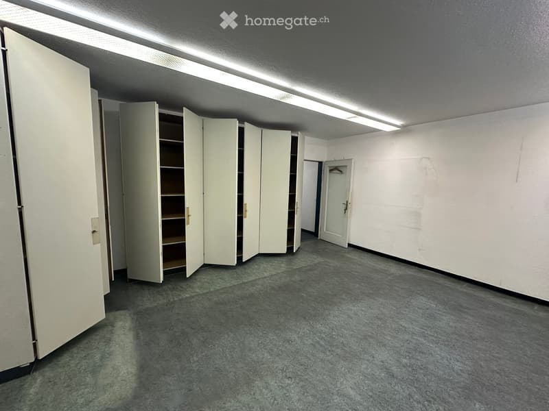 Empty room with grey concrete floor, white walls, and several open white storage cabinets with shelves.