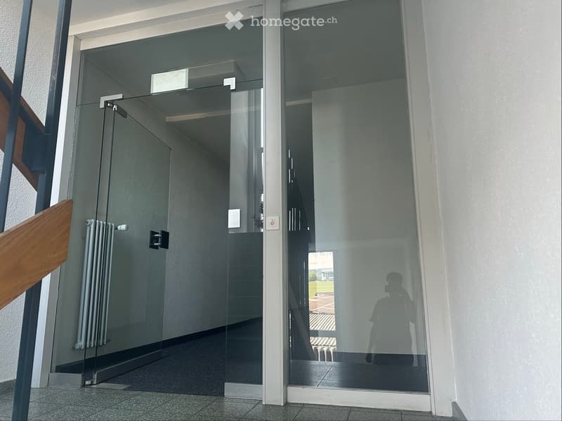 Modern hallway with glass doors, radiator, and tiled floor.