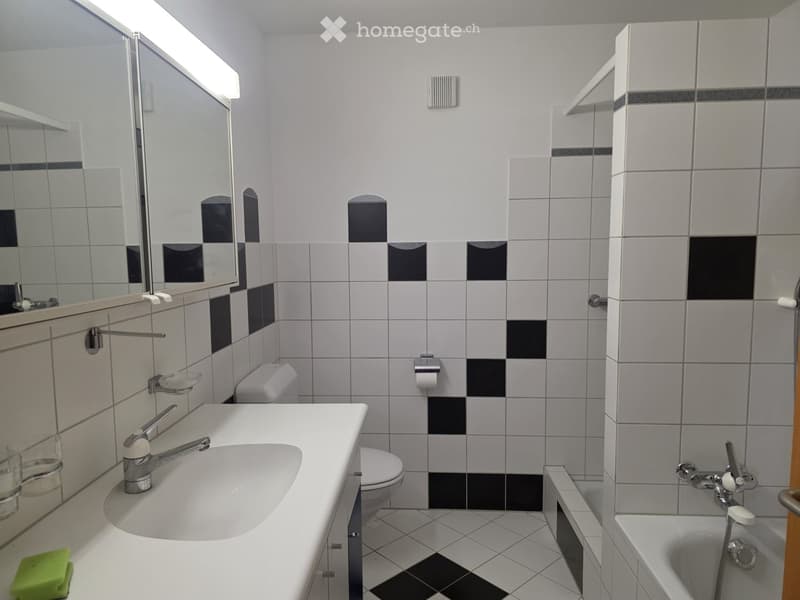 Modern bathroom with white and black tiled walls and floor, featuring a sink, toilet, bathtub, and large mirror.