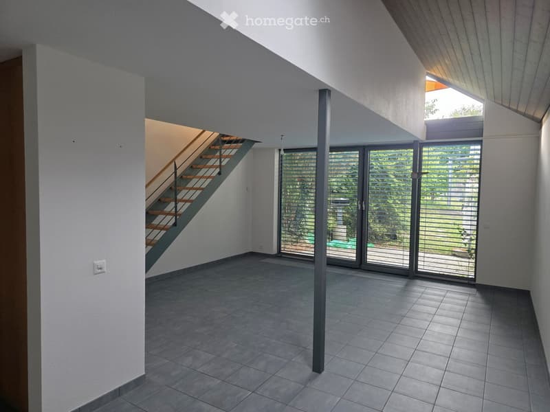 Modern, minimalist hallway with grey tiled flooring, white walls, a staircase leading upwards, and large glass doors opening to a garden area.