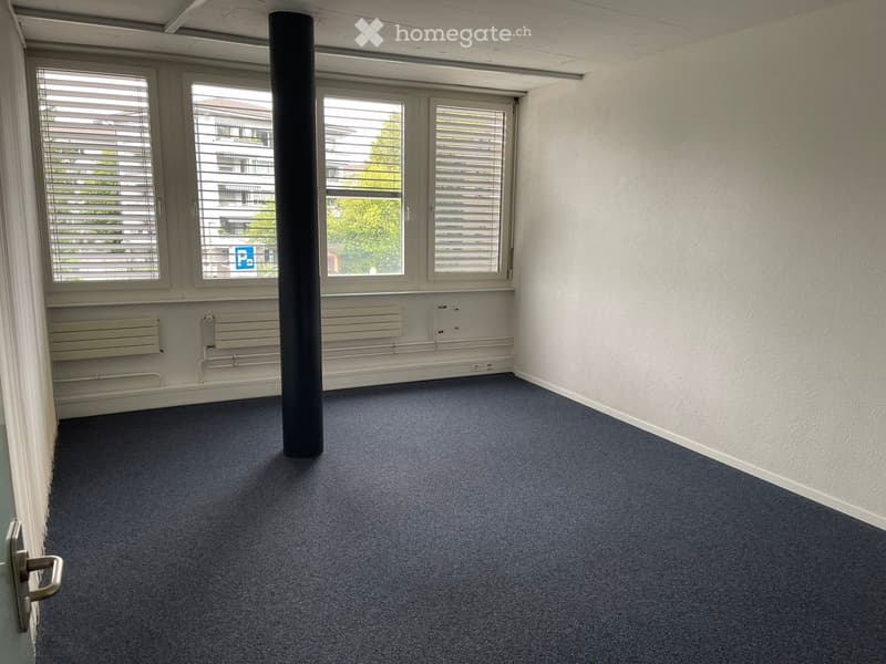 Empty room with blue carpet, white walls, large windows with blinds, and a central column.