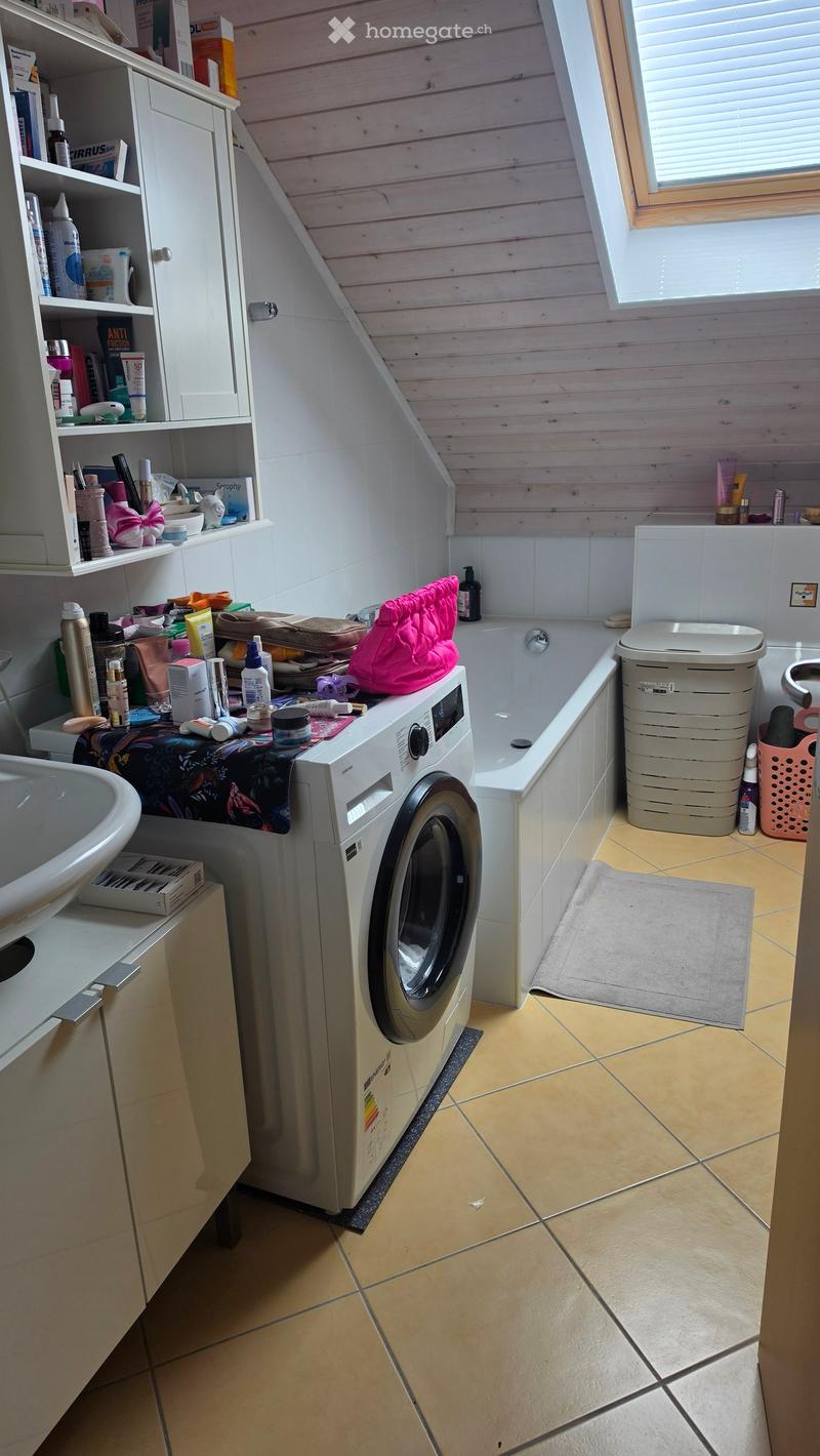 Bathroom with a washing machine, sink, bathtub, toilet, and shelves holding various toiletries.