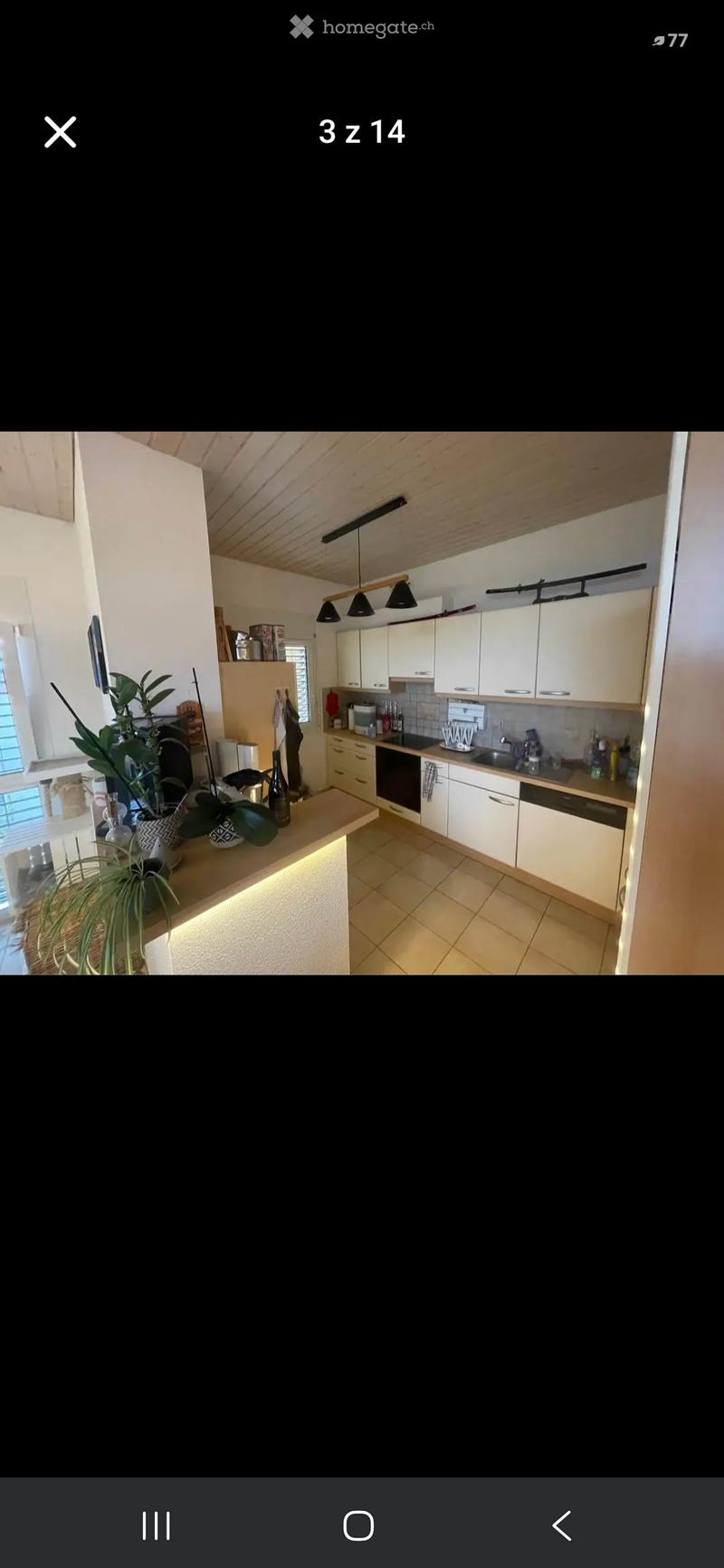 Modern kitchen with white cabinets, a central island with a built-in light, and various appliances including an oven and sink. The space features a tiled floor and a wooden ceiling with pendant lights.