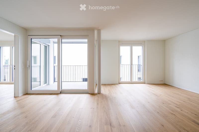 Empty room with light wooden flooring, white walls, large sliding glass doors leading to a balcony, and additional windows.