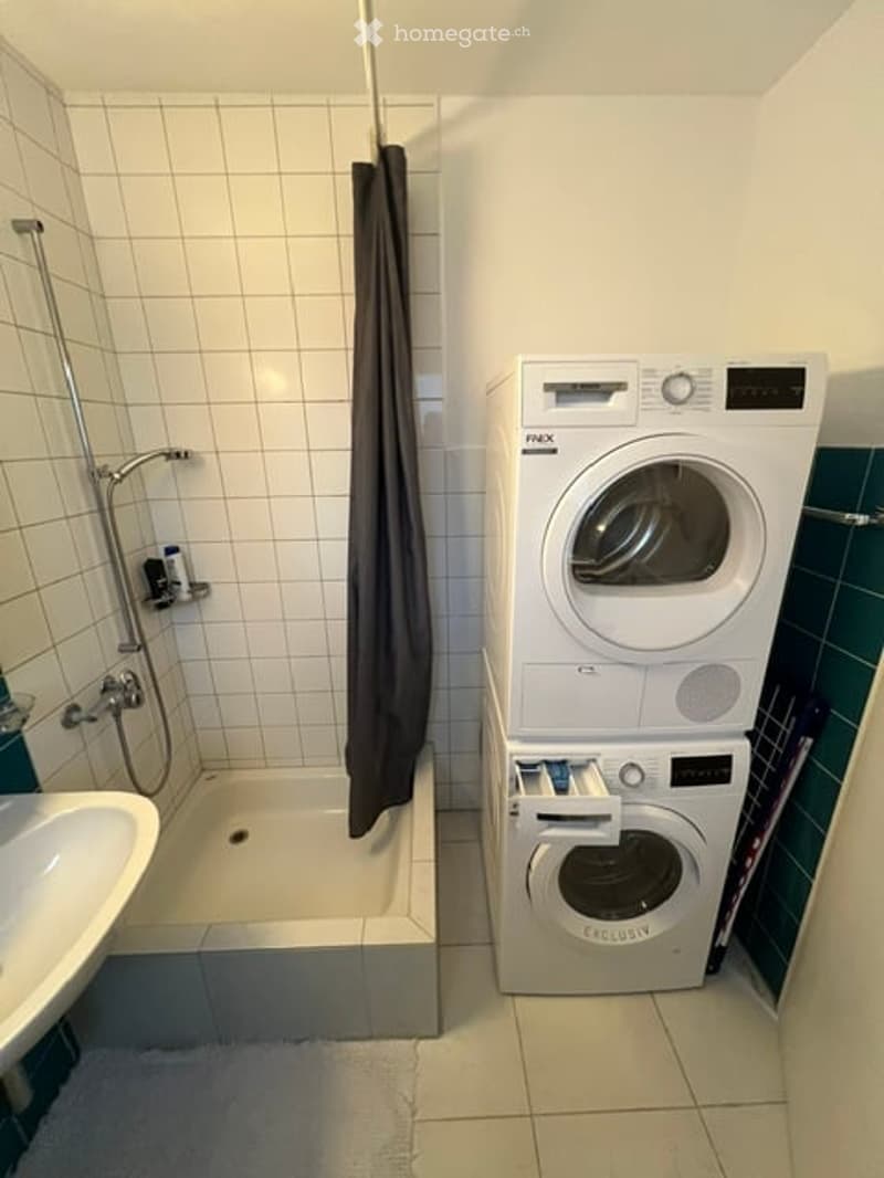 Compact bathroom with a shower, sink, and stacked washing machine and dryer unit.
