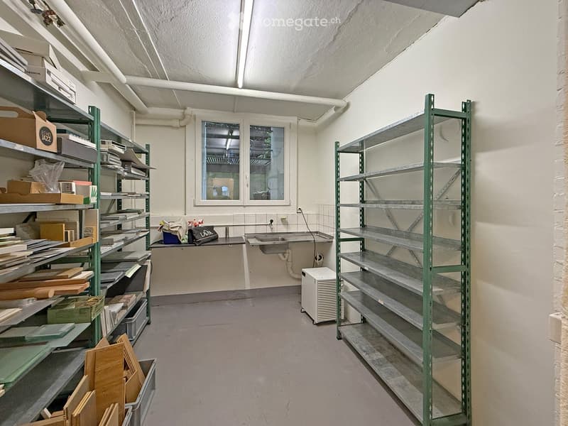 A storage or utility room with metal shelving units, a sink, and various storage boxes. The room has a concrete floor and white walls.