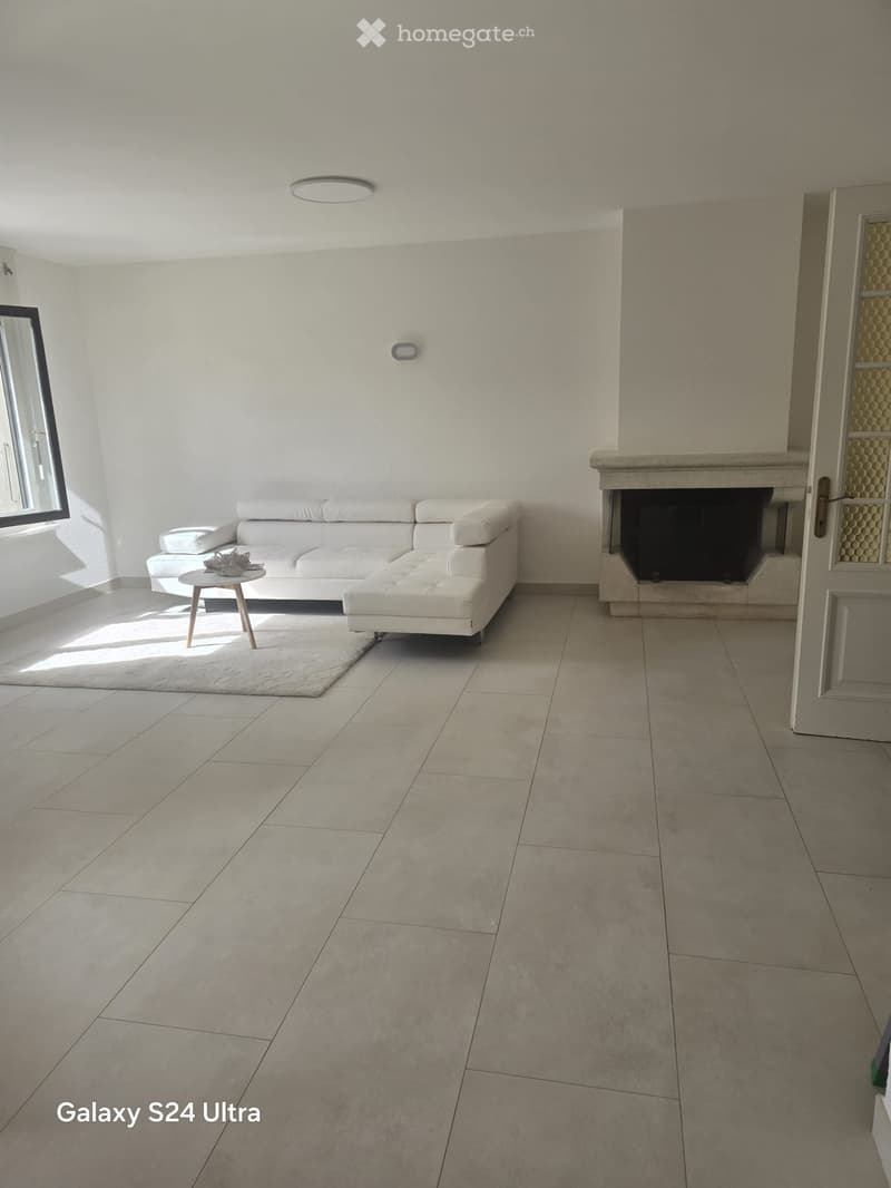 Modern living room with white walls, tiled floor, white sectional sofa, small coffee table, fireplace, and large window letting in natural light.