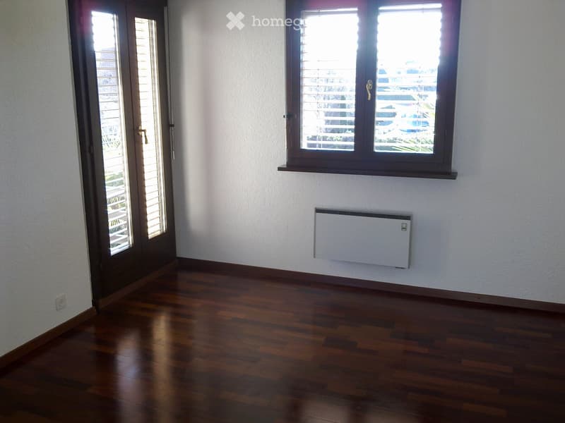 Empty room with wooden flooring, white walls, a window with blinds, and a radiator on the wall.