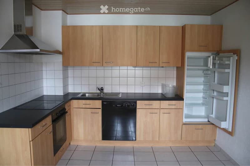Modern kitchen with light wooden cabinets, black countertops, stainless steel appliances including a refrigerator, dishwasher, and oven, and a sink with a faucet.