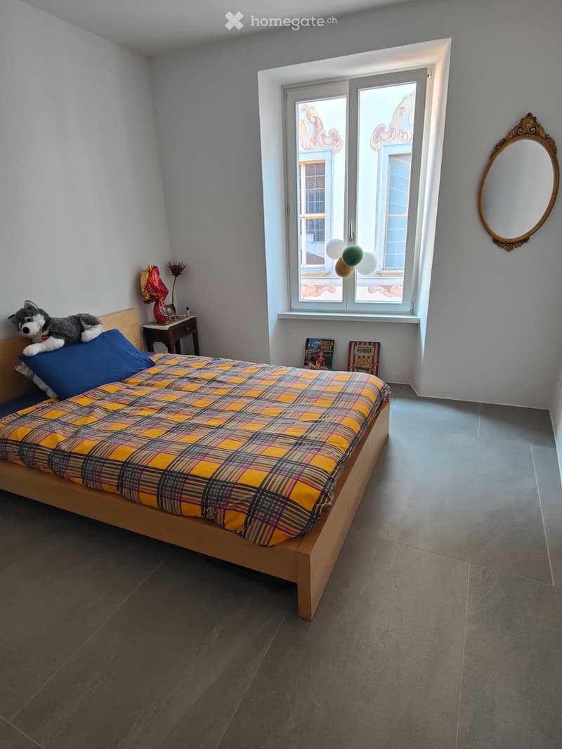 A cozy bedroom with a wooden bed, plaid bedspread, nightstand, mirror, and decorative items.
