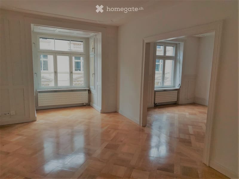 Empty room with wooden flooring, large windows, and radiators. No furniture or equipment present.