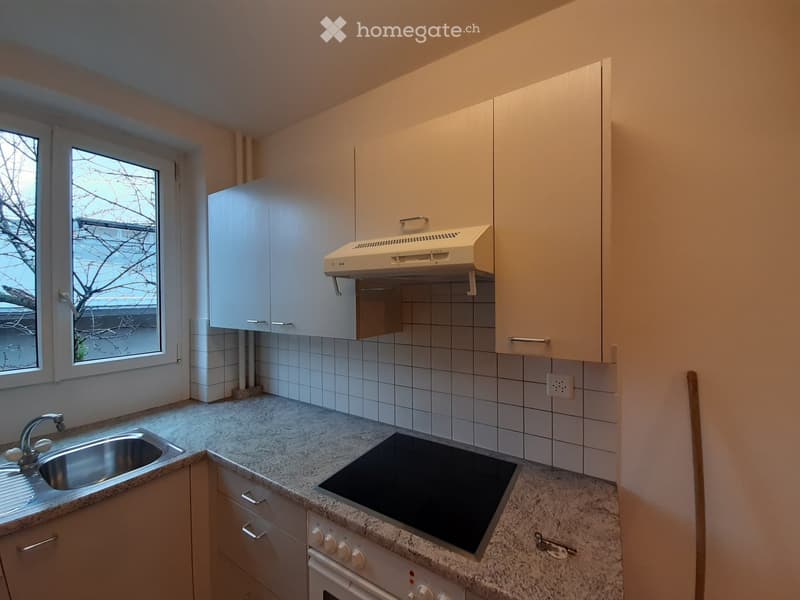 Modern kitchen with granite countertops, white cabinets, stainless steel sink, electric stove, and built-in range hood.