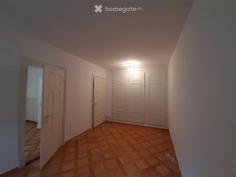 Empty hallway with wooden flooring, white walls, and several closed doors, including a large set of double doors and a single door leading to another room.
