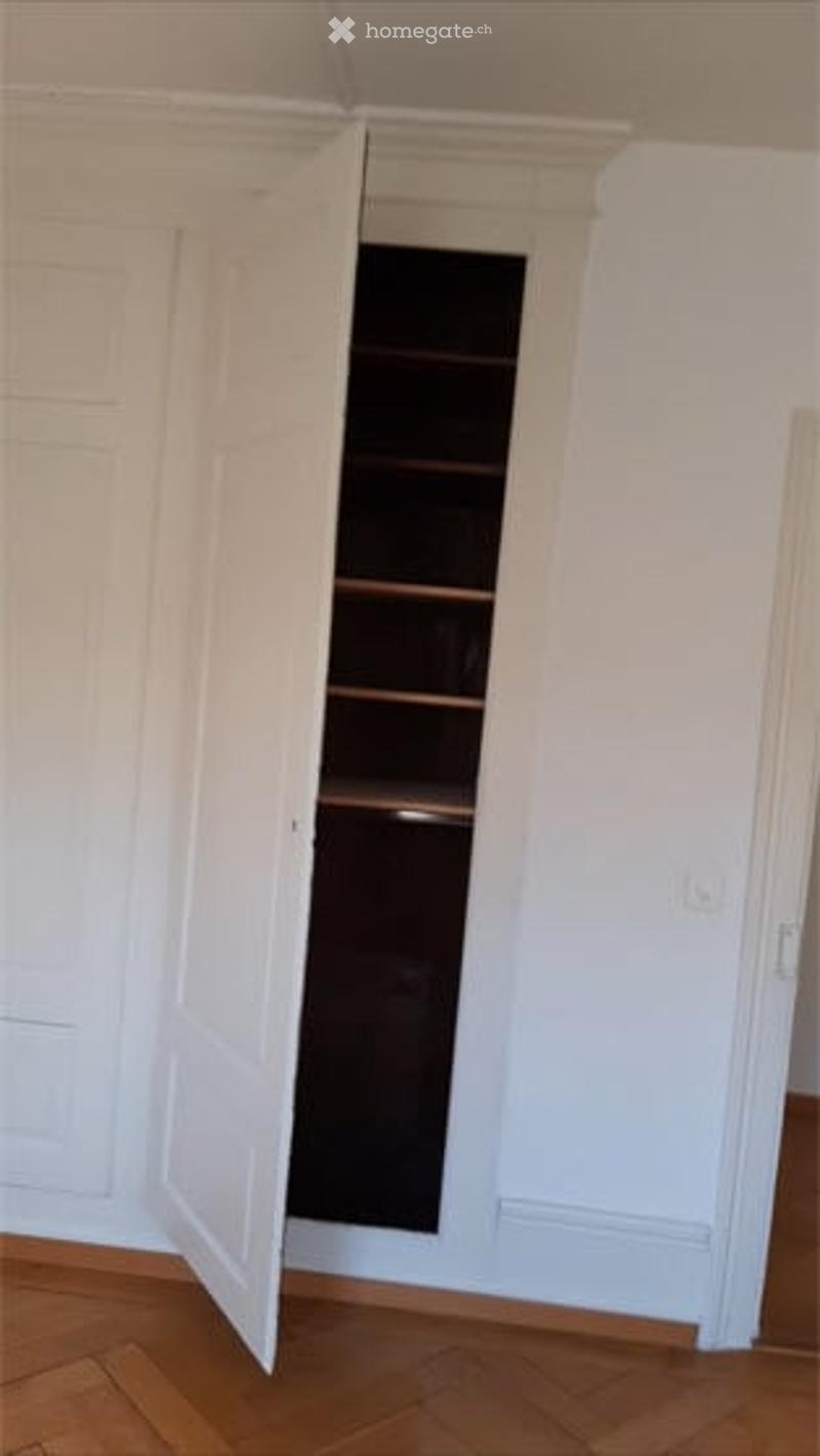 Empty room with light-colored walls, wooden flooring, and an open closet with empty shelves.