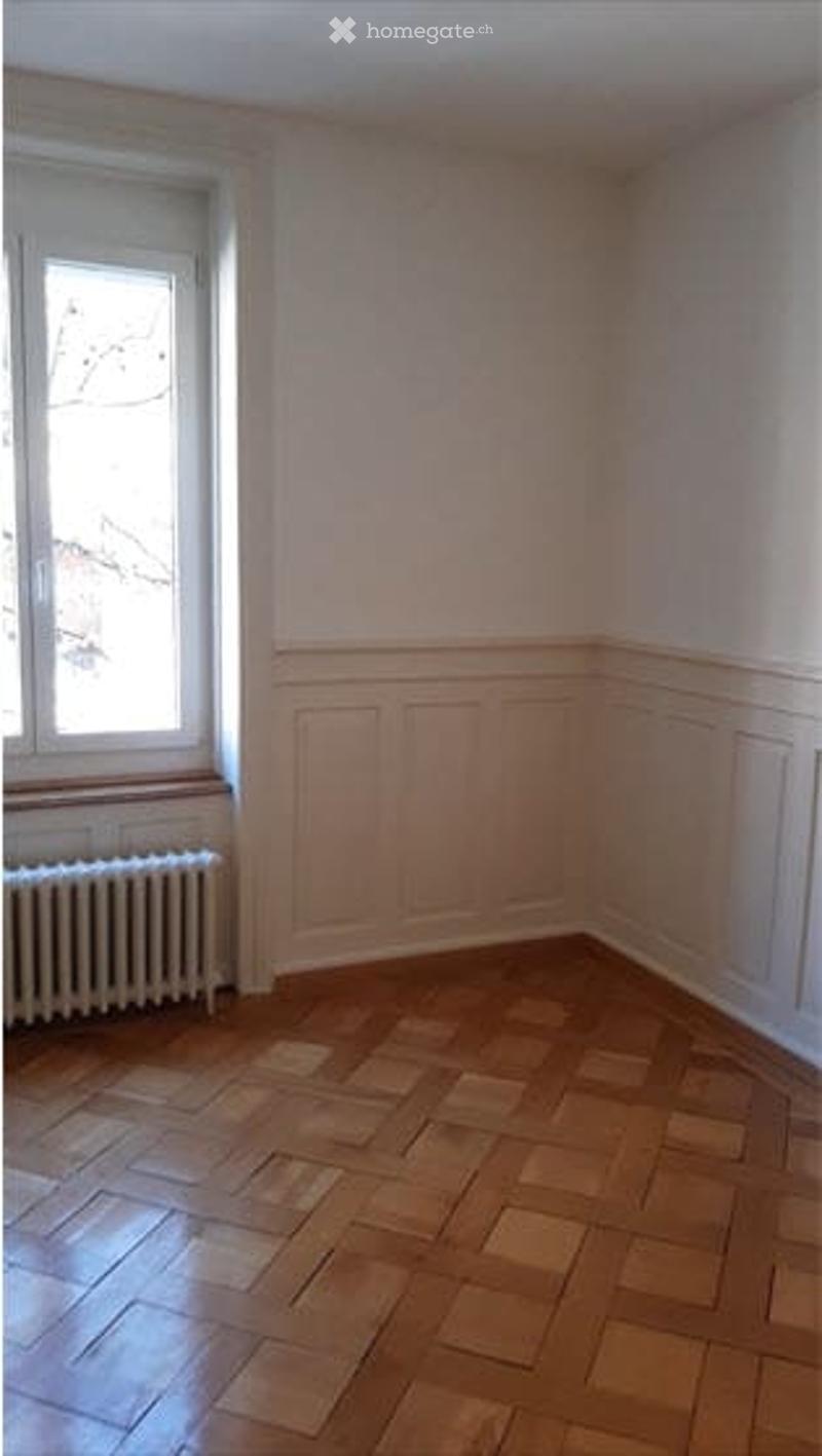 Empty room with wooden flooring, white walls, and a single window with a radiator below it.