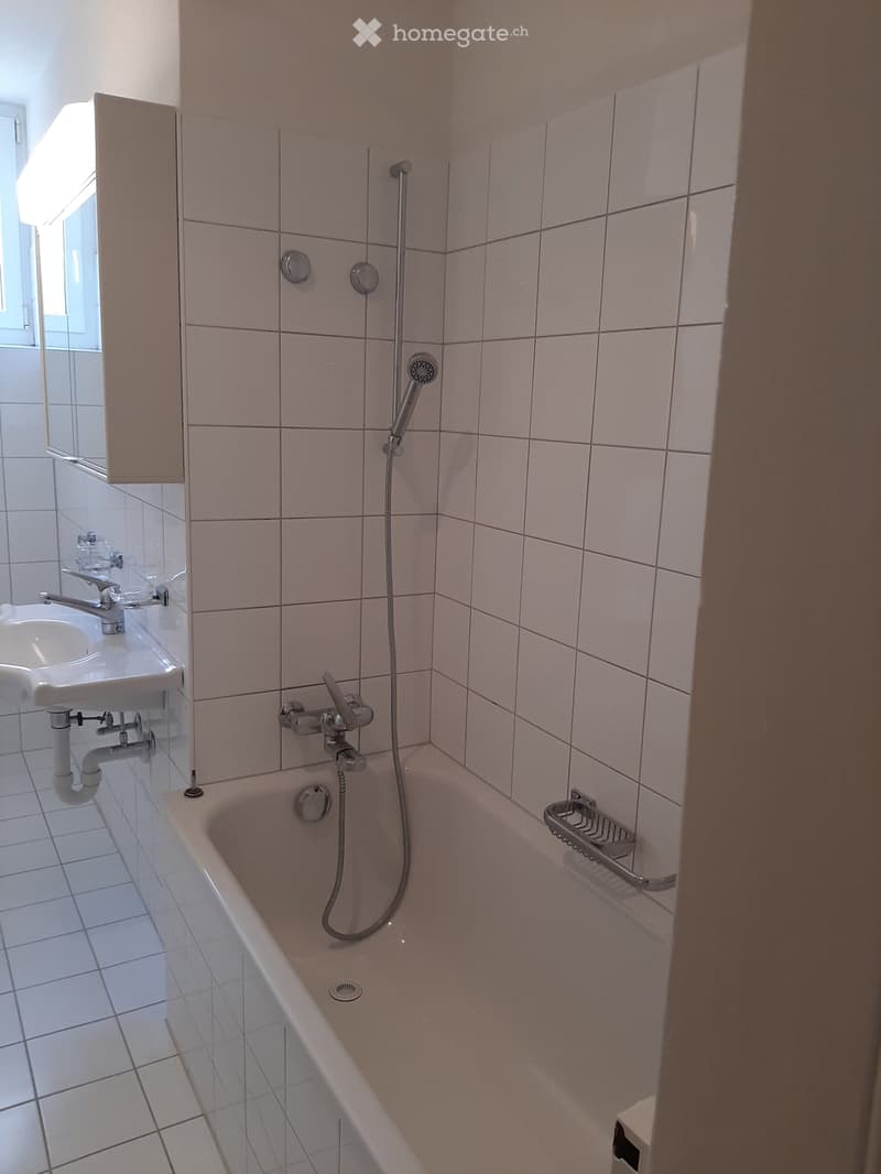 Bathroom with a bathtub, showerhead, sink, and mirror. Light pink tiles on walls and white tiles on the floor.