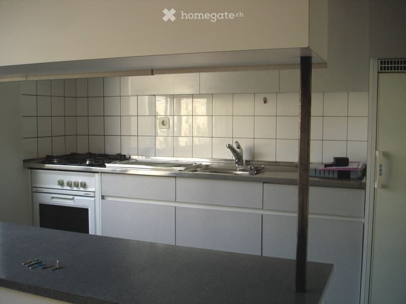 Modern kitchen with white cabinets, stainless steel sink, stove, and oven. Countertop has keys and small items.