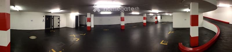 Underground parking area with marked parking spaces, red and white painted pillars, and overhead lighting.