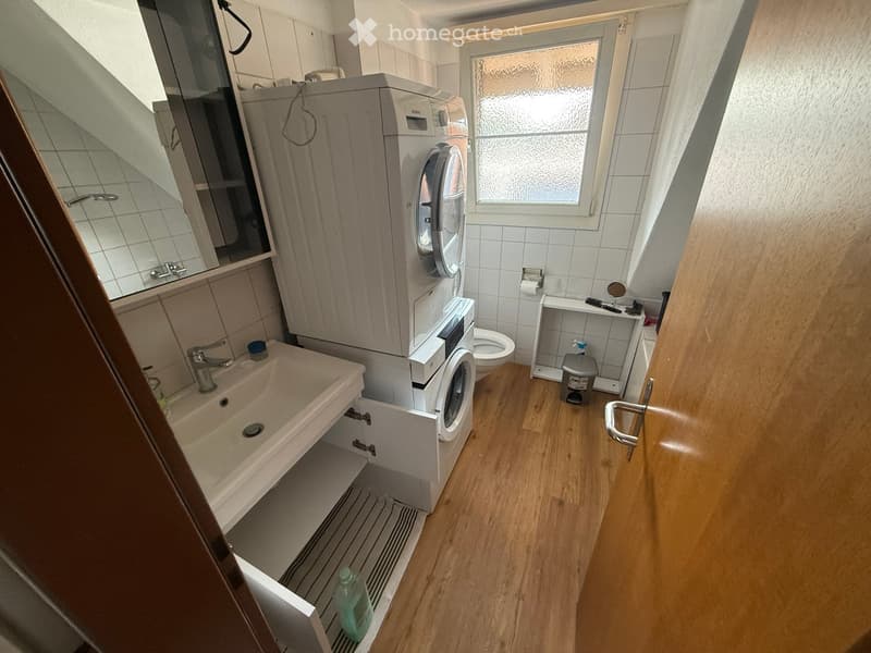 Bathroom with a sink, mirror, washing machine, toilet, and cabinet. Wooden flooring and tiled walls.