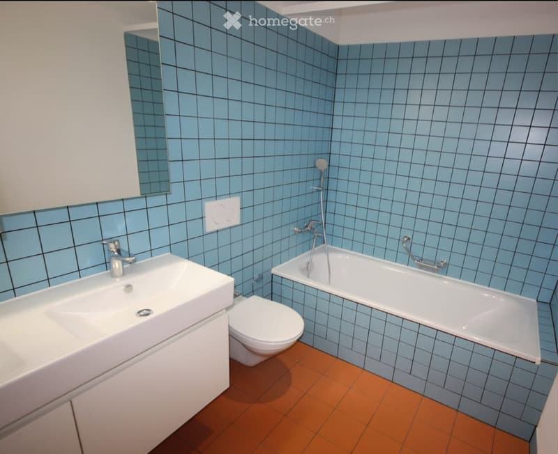 Modern bathroom with blue tiled walls, a white sink, toilet, bathtub, and a mirror above the sink.