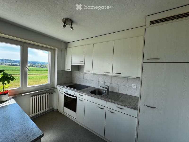 Modern kitchen with white cabinets, granite countertop, sink, oven, and a large window overlooking a green field.