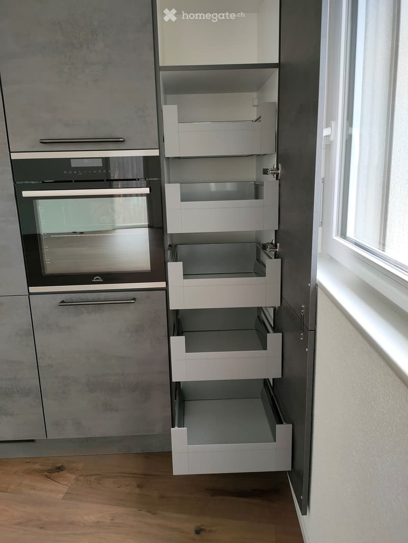 Modern kitchen with grey cabinets, an integrated oven, and open storage drawers.